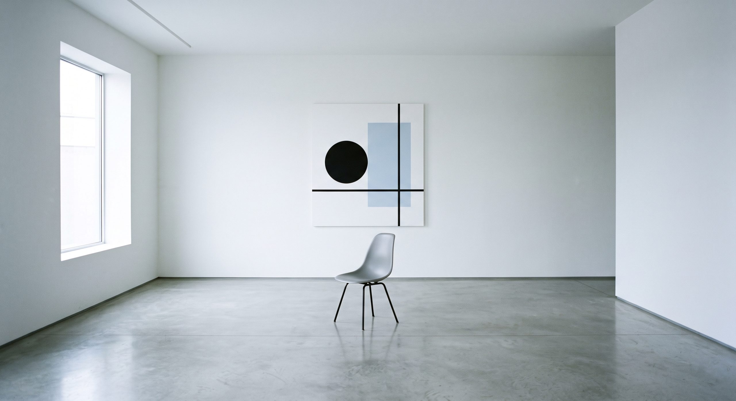 Stark minimalist interior with white walls, a single grey chair and one crisp geometric artwork