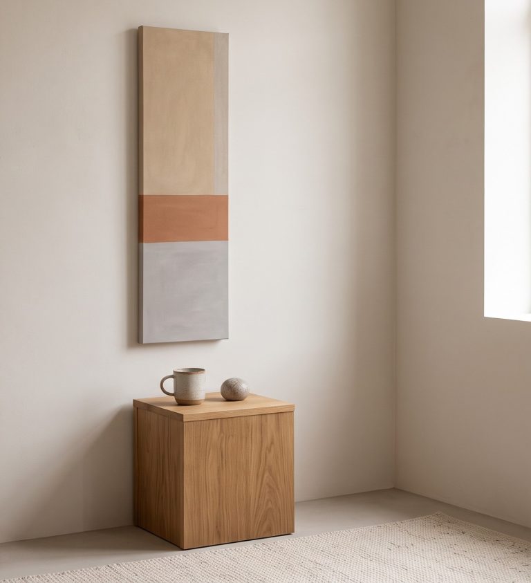 Compact studio corner with a tall narrow vertical minimalist artwork above a small oak side table
